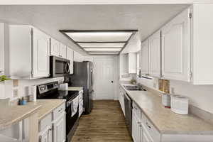 Kitchen with stainless steel appliances, a textured ceiling, white cabinetry, light countertops, and dark wood-style flooring