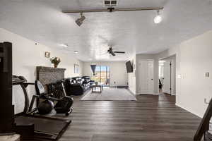 Living area with track lighting, dark wood-style floors, a textured ceiling, ceiling fan, and a brick fireplace