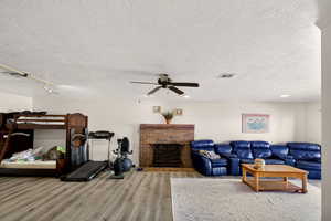 Living room with light wood-style floors, a textured ceiling, a brick fireplace, and a ceiling fan