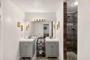 Bathroom featuring a walk in shower, two vanities, and a textured ceiling