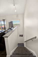 Stairway with plenty of natural light, rail lighting, and a textured ceiling