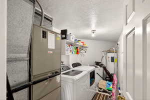 Laundry room featuring a textured ceiling, heating unit, washer and dryer, and electric water heater