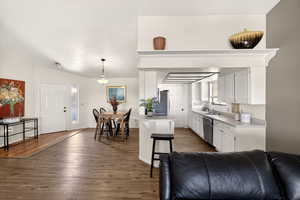 Kitchen featuring light countertops, white cabinetry, dark wood-type flooring, a kitchen breakfast bar, and stainless steel appliances