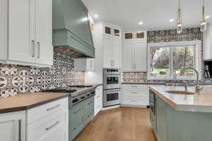Two tone kitchen with pendant lighting, glass insert cabinets, stainless steel appliances, dark stone counters, and dual tone cabinets