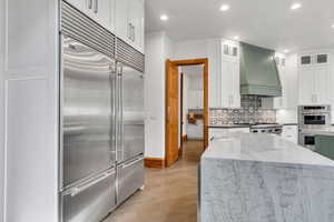 Two tone kitchen with stainless steel appliances, light stone counters, recessed lighting, dual tone cabinetry, and light wood finished floors