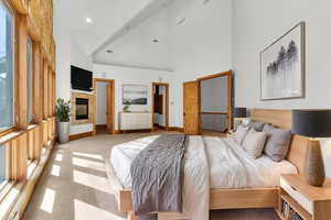 Bedroom featuring light colored carpet, a multi sided fireplace, a high ceiling, and recessed lighting (virtual stanging)