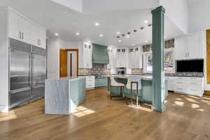 Two tone kitchen with dual tone cabinetry, stainless steel appliances, dark stone counters, light wood-style floors, and a breakfast bar area