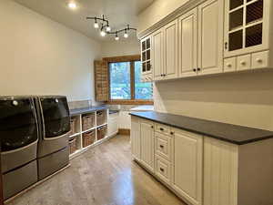 Laundry room featuring light wood-style flooring, separate washer and dryer, a textured ceiling, and cabinet space