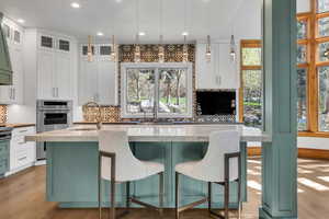 Dual tone kitchen with dual tone cabinetry, a kitchen island with sink, backsplash, a kitchen bar, and decorative light fixtures