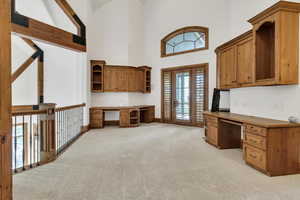 Unfurnished office featuring built in study area, light colored carpet, and a high ceiling