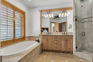 Bathroom with double vanity, a stall shower, a bath, a ceiling fan, and stone tile floors