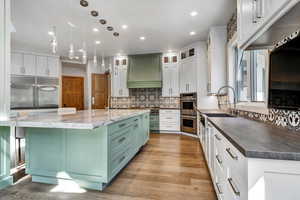 Kitchen with dual tone cabinetry, a large island with sink, stainless steel appliances, pendant lighting, and glass fronted cabinets