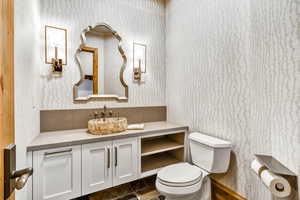 Half bath with wallpapered walls, vanity, and dark stone finish flooring
