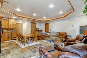 Living area featuring a tray ceiling, ornamental molding, stone tile floors, and recessed lighting