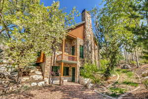 Rear view of property with stone siding, a chimney, a balcony, and a patio area