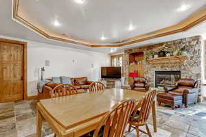 Dining space with a fireplace, light stone finish floors, a raised ceiling, ornamental molding, and recessed lighting