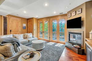 Living area with a glass covered fireplace, light wood-style flooring, recessed lighting, and french doors