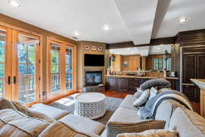 Living area with beamed ceiling, dark wood-style floors, a glass covered fireplace, recessed lighting, and french doors