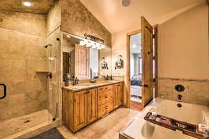 Ensuite bathroom featuring a bath, lofted ceiling, double vanity, a stall shower, and light tile patterned flooring