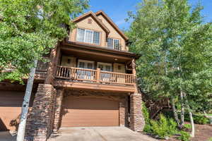 View of front of house with stone siding, driveway, an attached garage, and covered porch