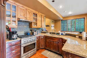 Kitchen with stainless steel range with gas cooktop, glass fronted cabinets, light stone countertops, decorative backsplash, and light wood-style floors