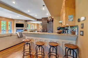 Kitchen with light stone countertops, a peninsula, a breakfast bar area, light wood-style flooring, and recessed lighting