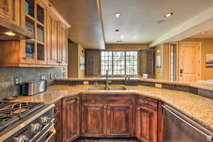 Kitchen with stainless steel appliances, glass fronted cabinets, light stone countertops, recessed lighting, and extractor fan