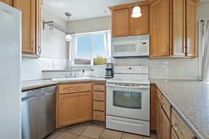 Kitchen with white appliances, pendant lighting, light tile patterned floors, and wood finish cabinets