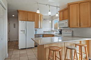 Kitchen with white appliances, a peninsula, a breakfast bar area, tasteful backsplash, and light tile patterned floors
