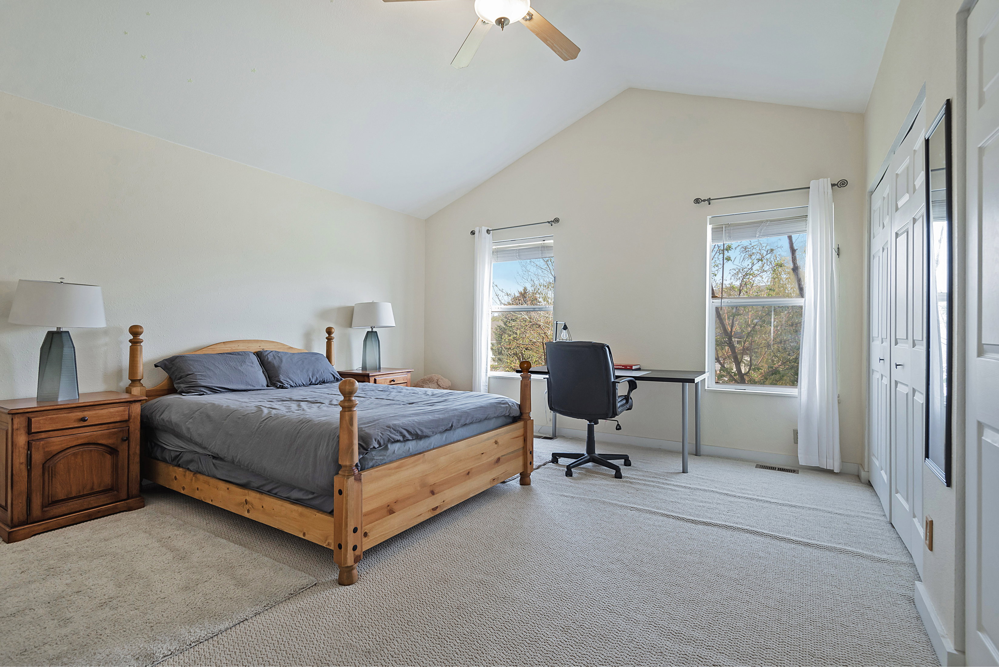 Bedroom with light colored carpet, a ceiling fan, a closet, and a desk