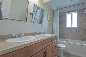 Full bathroom featuring a textured wall, double vanity, and shower / tub combo with curtain