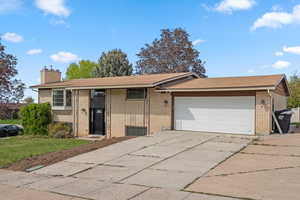 Split foyer home featuring concrete driveway, a garage, brick siding, roof with shingles, and a chimney