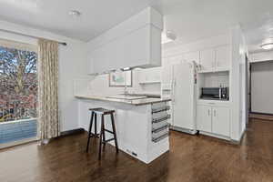 Kitchen with white fridge with ice dispenser, a kitchen breakfast bar, a peninsula, white cabinets, and dark wood finished floors