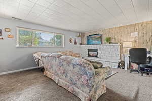 Carpeted living room featuring a fireplace, wood walls, and a desk