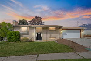 View of front of property with a lawn, a garage, concrete driveway, brick siding, and a chimney