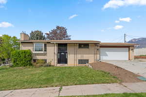 Raised ranch featuring brick siding, driveway, a garage, a front yard, and a chimney