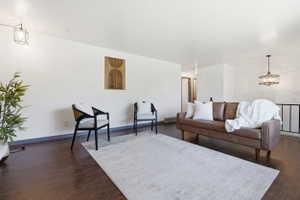 Spacious living area featuring dark wood-finish flooring, white walls, and a contemporary chandelier