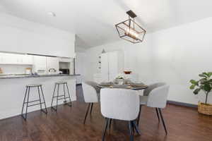 Open-concept dining area featuring dark wood-finish flooring, a contemporary black metal chandelier, and white baseboards