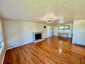 Unfurnished living room featuring light wood-style flooring, a brick fireplace, and a textured ceiling