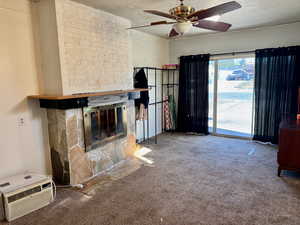 Unfurnished living room with carpet flooring, a large fireplace, a ceiling fan, and a textured ceiling
