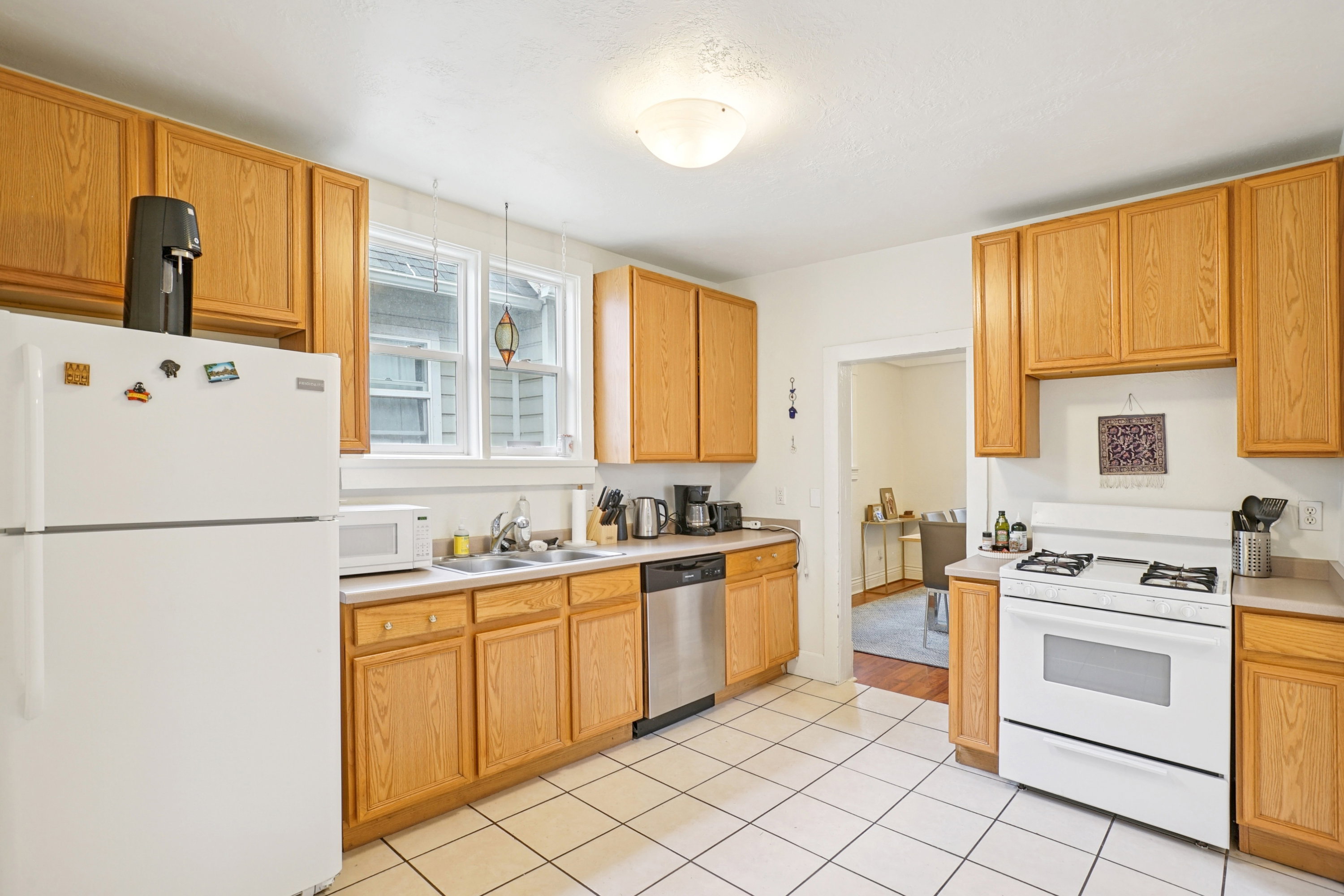 Kitchen featuring white appliances, light countertops, light tile patterned flooring, and light wood finish cabinetry