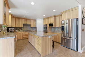 Kitchen featuring light wood finish cabinets, stainless steel appliances, light stone counters, light tile patterned floors, and recessed lighting