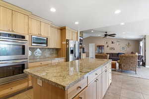 Kitchen featuring light wood finish cabinets, stainless steel appliances, lofted ceiling, tasteful backsplash, and open floor plan