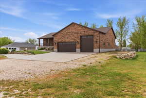 View of property exterior with driveway, a garage, brick siding, and a lawn