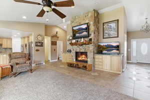 Living area featuring lofted ceiling, a ceiling fan, light tile patterned flooring, light colored carpet, and a stone fireplace