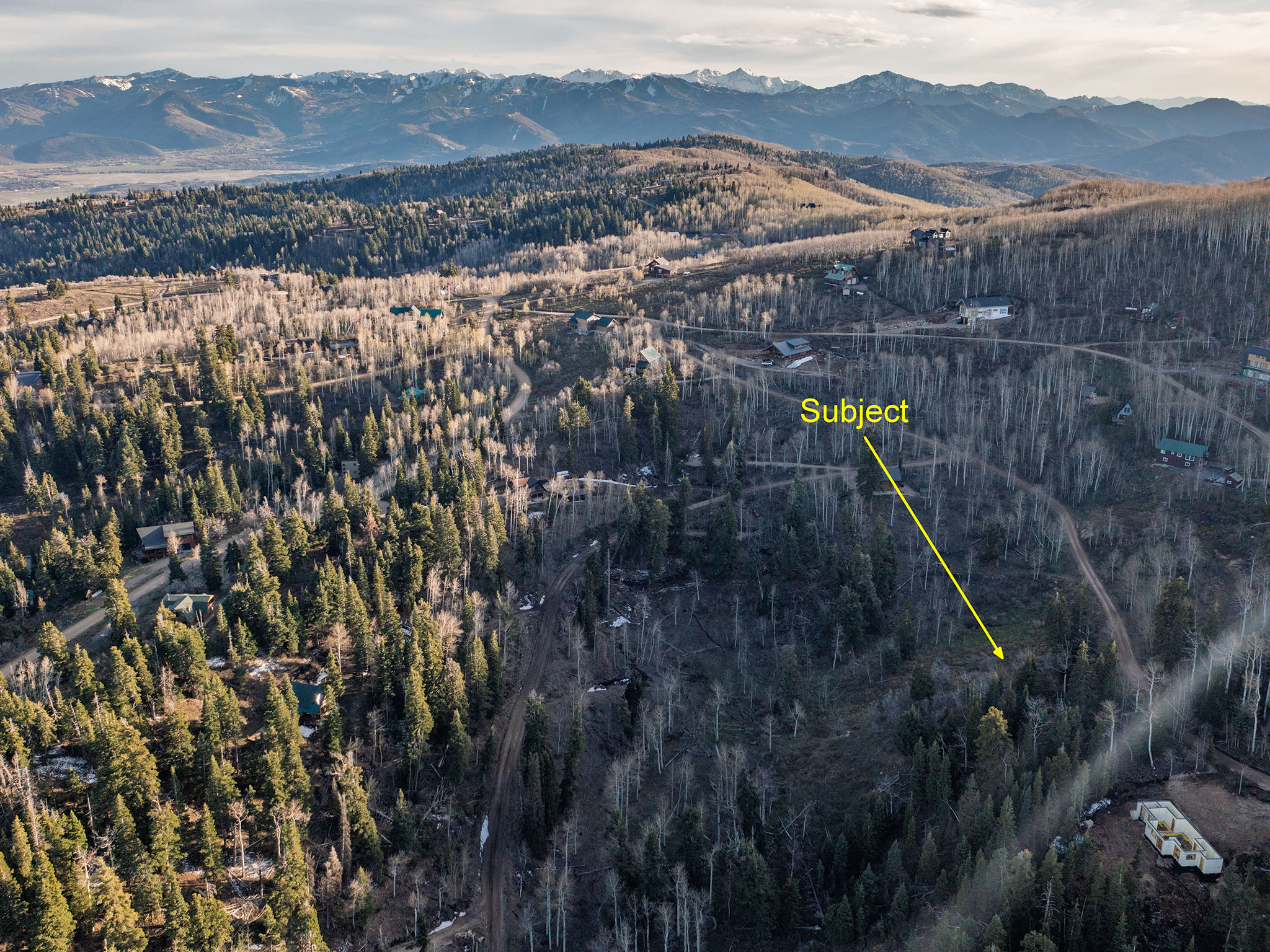 Aerial overview of property's location with a mountainous background and a heavily wooded area