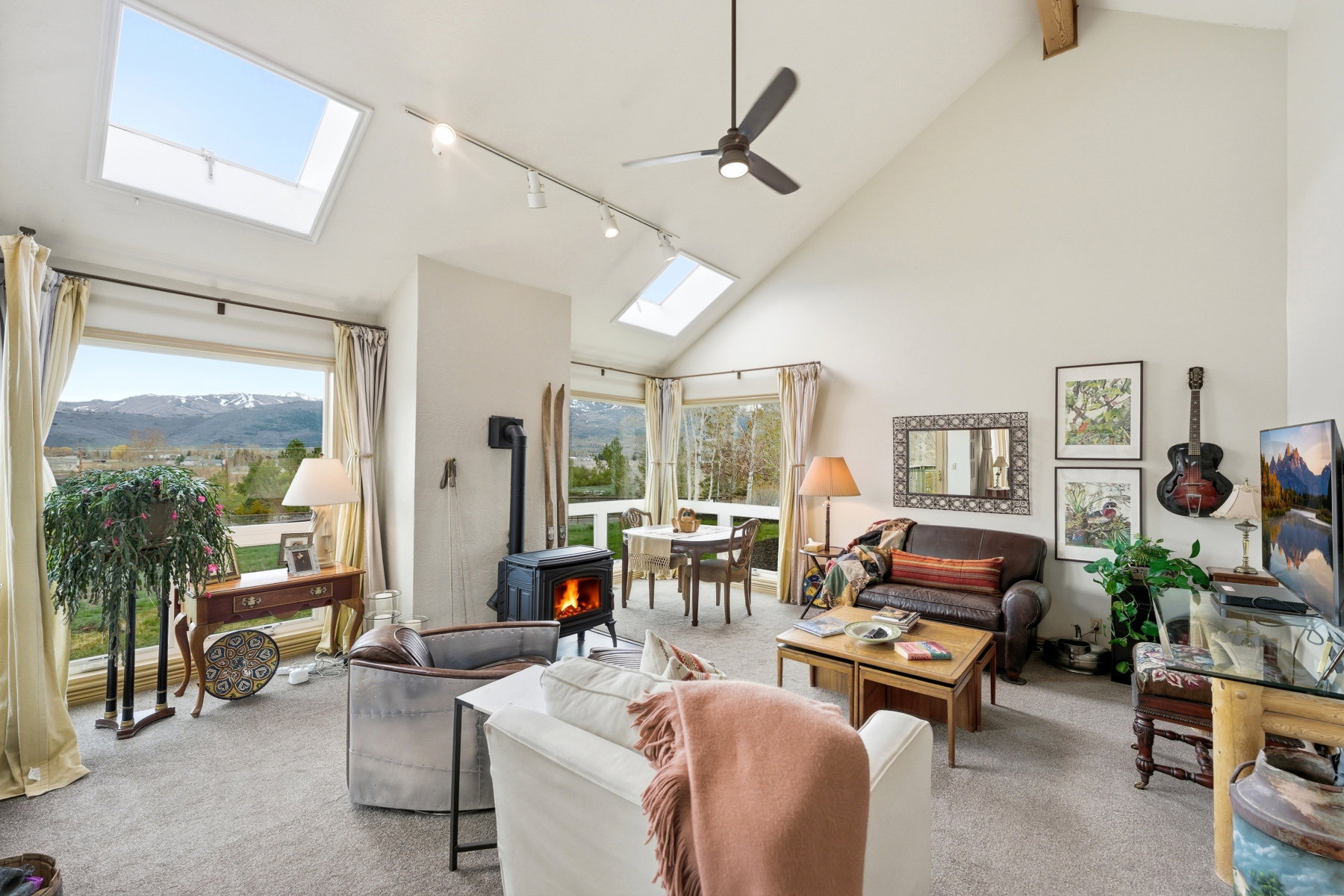 Living area with a wood stove, carpet, lofted ceiling, rail lighting, and a skylight