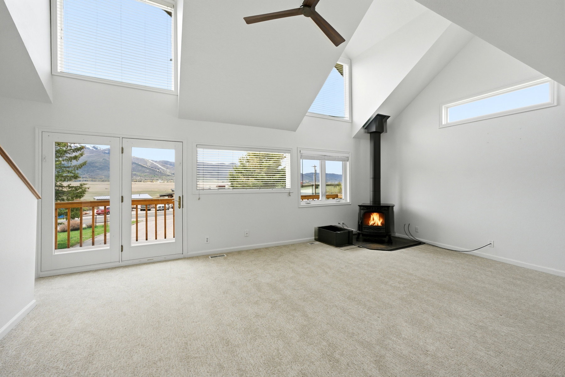 Unfurnished living room featuring a wood stove, carpet floors, ceiling fan, and lofted ceiling
