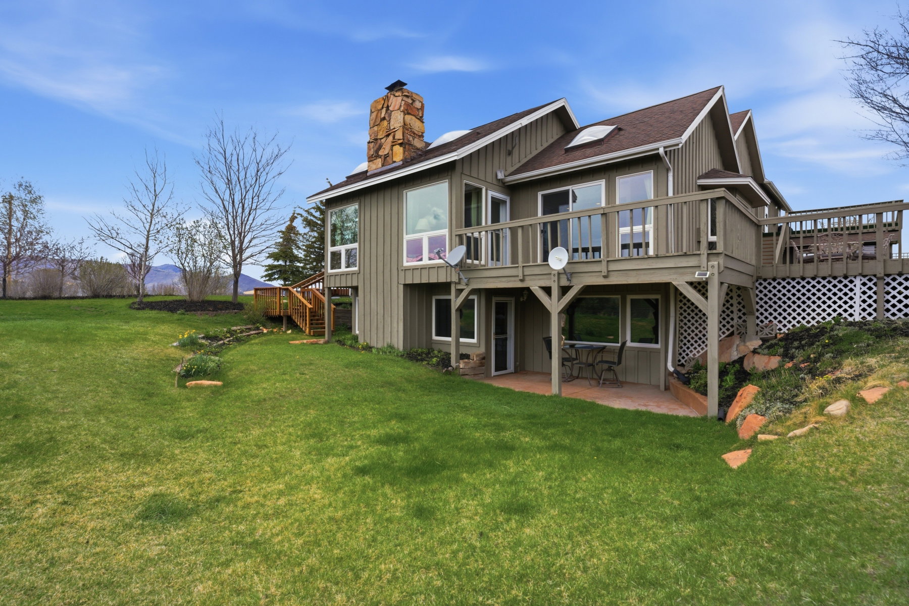 Back of property with a wooden deck, a patio, a lawn, a chimney, and board and batten siding