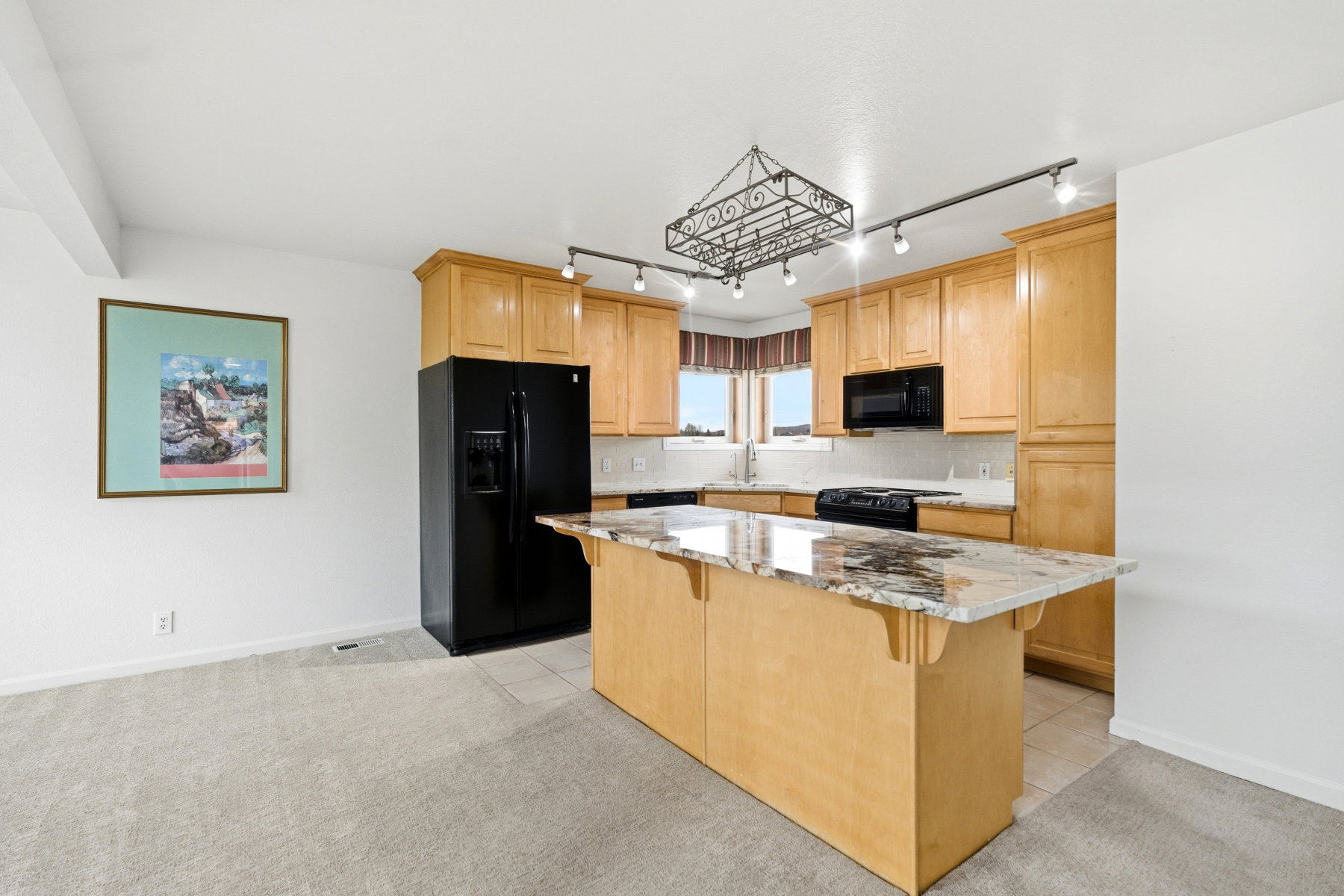 Kitchen with black appliances, light wood finish cabinets, a breakfast bar area, light tile patterned flooring, and track lighting